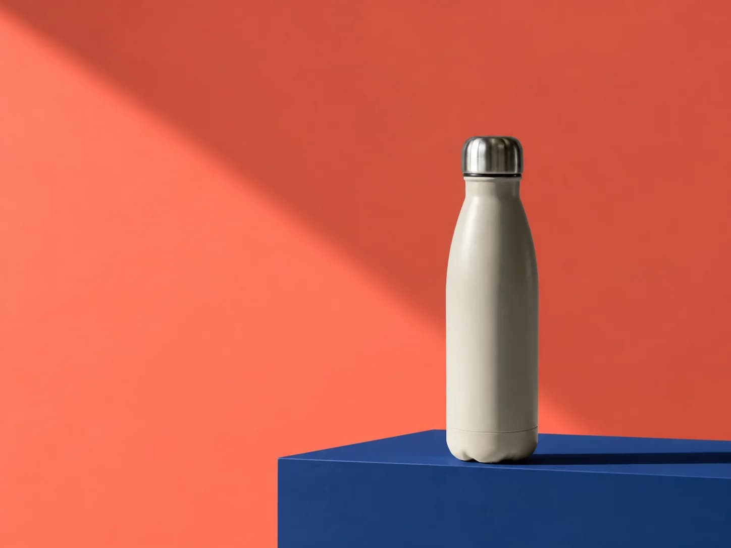 Cream bottle unchanged on a blue plinth against a coral background
