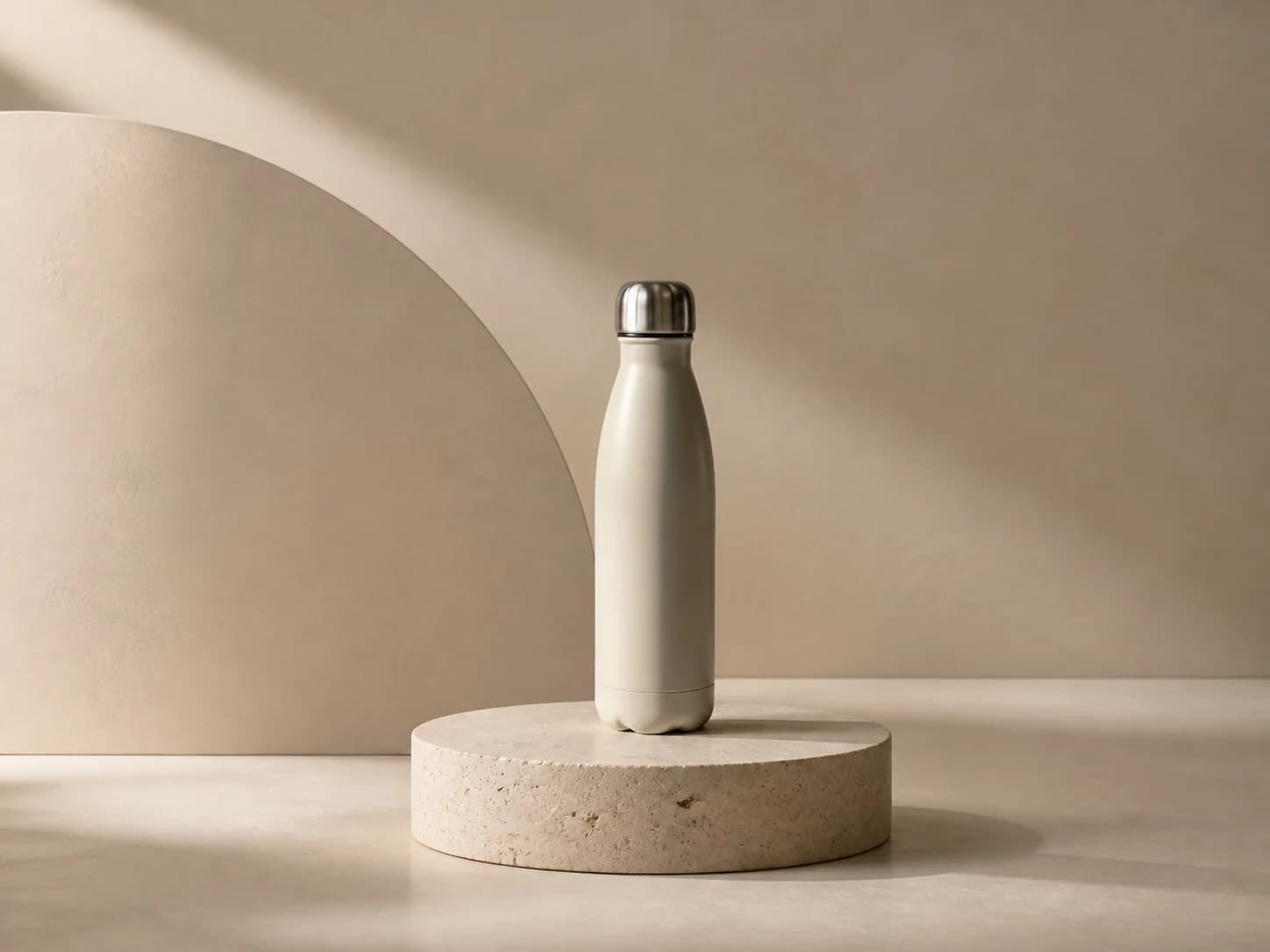 Cream bottle unchanged on a travertine pedestal in a warm plaster set